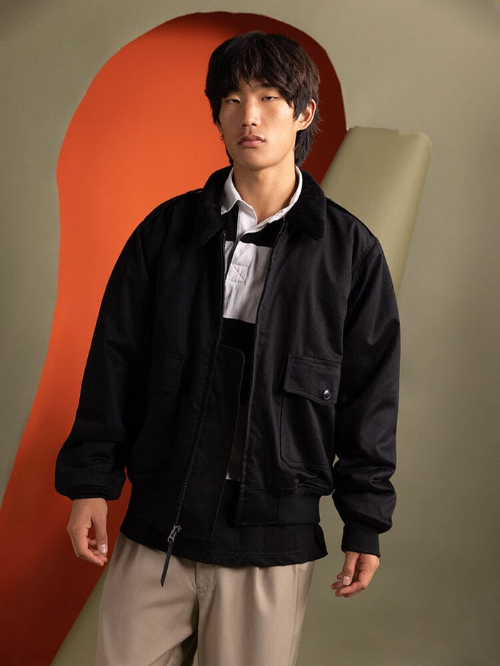 A person wearing the 1940s B-10 Bomber Jacket in black by Alpha Industries over a white shirt.