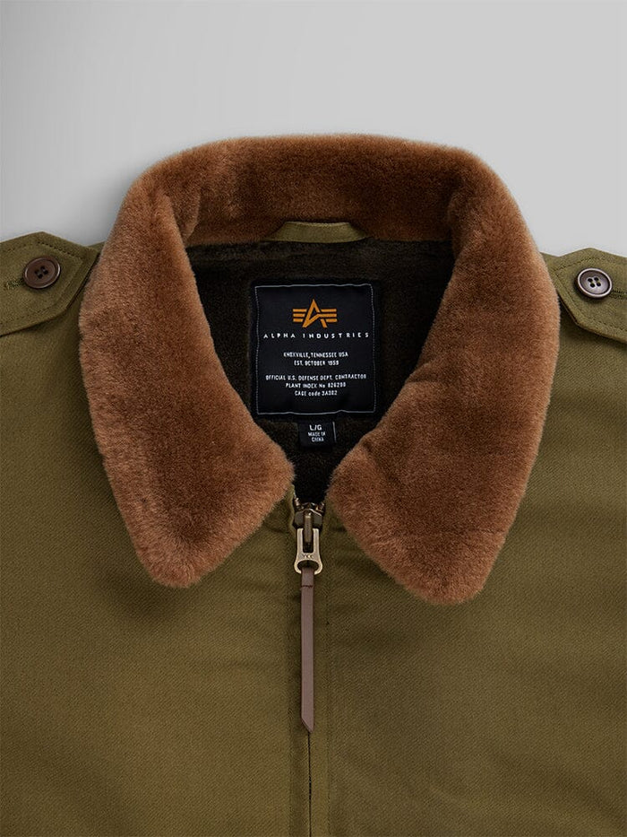 A 1940s B-10 bomber jacket featuring a retro-style olive green design and a brown faux fur collar with a zip closure. The label displays Alpha Industries and includes care instructions.