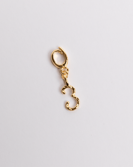 A gold-colored charm in the shape of the number 3 with a small loop attachment, displayed against a white background.