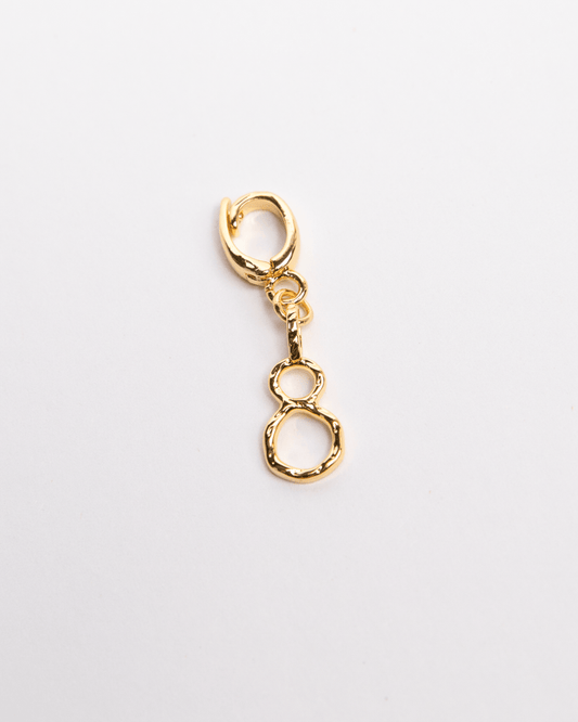 A gold-colored charm in the shape of the number 8 with a small clasp attached, displayed against a white background.