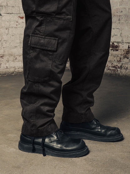 Alpha Industries Acu Pant black cargo pants with utility pockets, paired with black leather shoes.