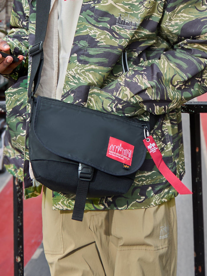 Alpha X Manhattan Portage Nylon Messenger Bag SM by Alpha Industries in green camo, flight nylon material, red logo patch, hi-vis rescue orange keychain strap.