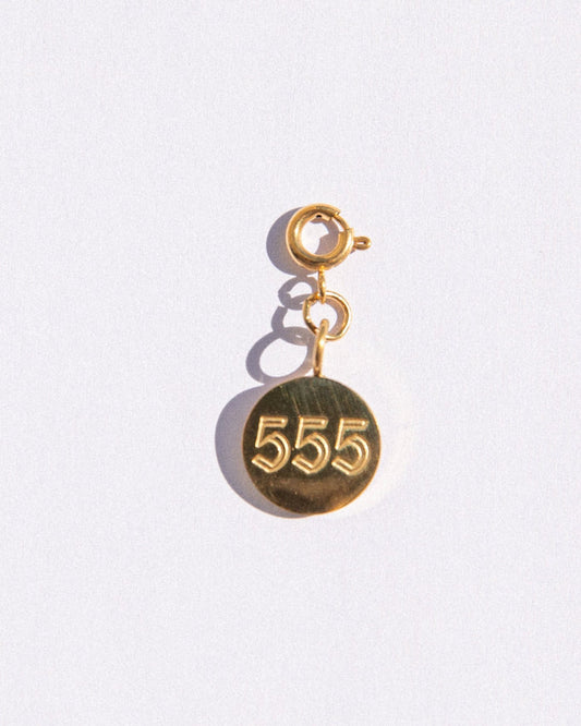 Gold circle charm with angel numbers '555' on a white background