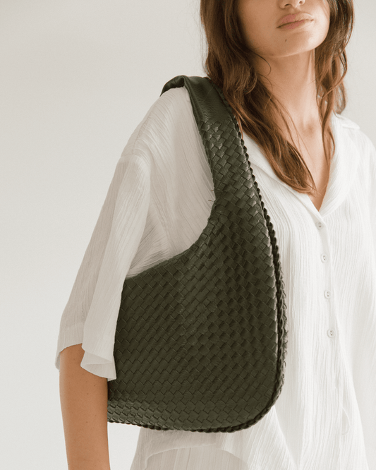 Person wearing a green woven bag on a plain background