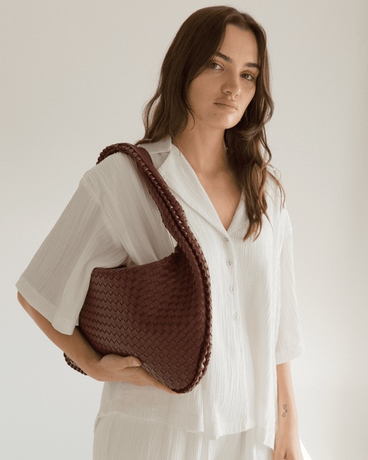 Woman holding a maroon woven handbag against a plain background