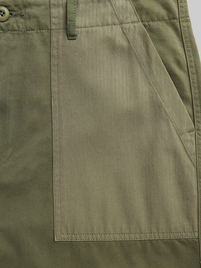 Alpha Industries Fatigue Pant in olive green cotton with large front utility pocket, visible stitching, and button near waistband.