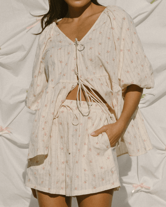 Woman wearing a delicate cream coloured shirt with pink flowers and matching shorts.