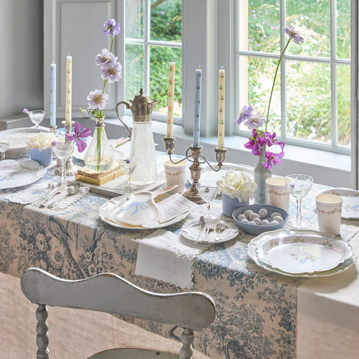 Elegant dining table setting with floral arrangements, candles, and decorative items in a bright room.