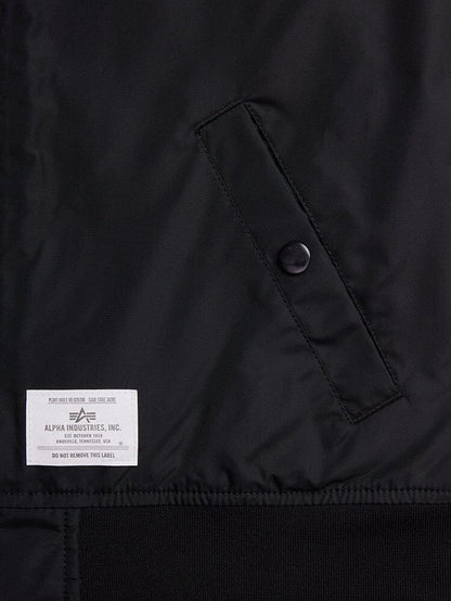 Close-up of a black fabric with a buttoned pocket and a white label reading Alpha Industries, Inc. The L-2B Skymaster Gen II Bomber Jacket W is made from lightweight nylon, offering water-resistant properties and featuring intricate oxygen tab details for enhanced functionality.