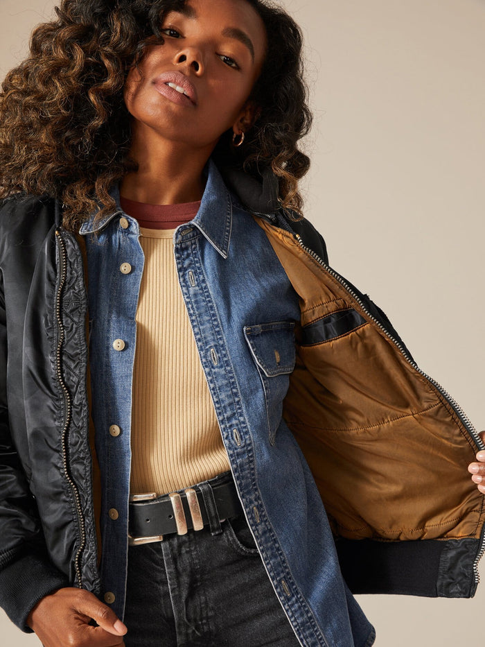A person wearing an Alpha Industries MA-1 Hooded Battlewash Bomber Jacket over a denim shirt and beige top, stylishly showcasing the inside lining.