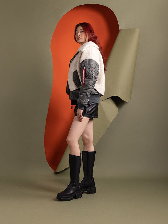 Side-view of a person wearing the Women's B-15 Sherpa Hybrid Bomber Jacket by Alpha Industries, styled in a mix of white and gray with an asymmetrical zipper.