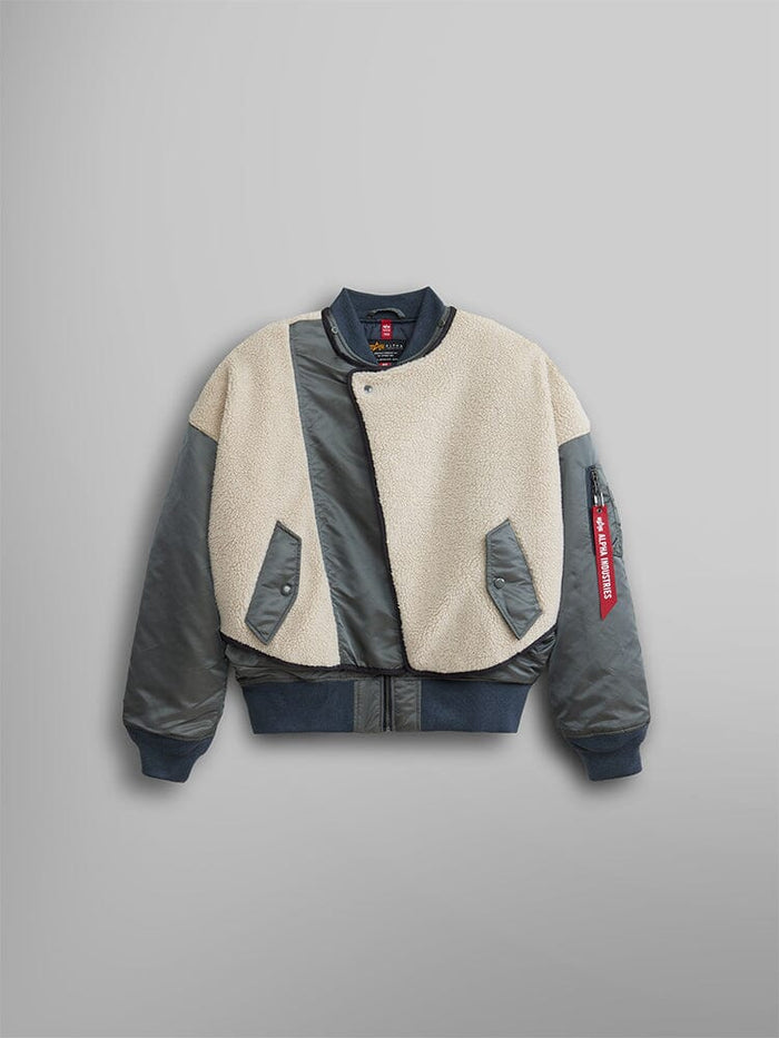 The Alpha Industries Women's B-15 Sherpa Hybrid Bomber Jacket features dark sleeves with a cream faux-shearling front, sherpa paneling, snap buttons, and a distinctive red tag on the sleeve.