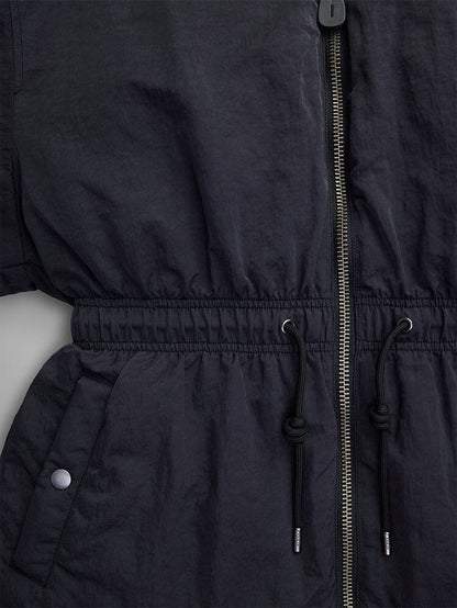 Close-up of the Alpha Industries Women's Short Cinched Waist Jacket in black nylon, showcasing a zipper, adjustable drawcord waist, and welt pockets. The design is enhanced with buttoned details and a cozy quilted lining.